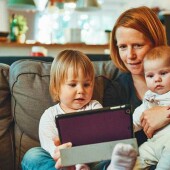 A mother and her children sit together on a couch in a cozy living room with a tablet